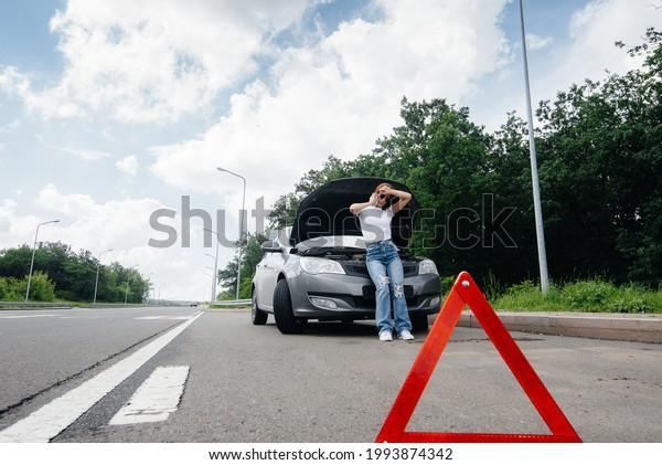 A young girl stands near a\
broken-down car in the middle of the highway and calls for help on\
the phone. Failure and breakdown of the car. Waiting for\
help.