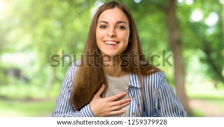 Young girl with striped shirt smiling a lot while putting hands on chest at outdoors