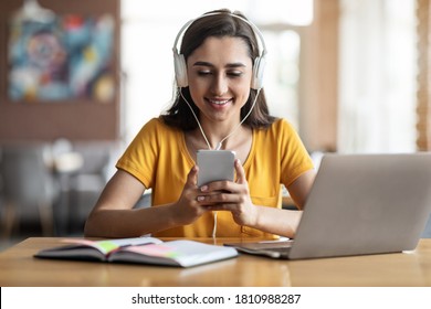 Young girl student in headset sitting at cafe, using laptop and smartphone