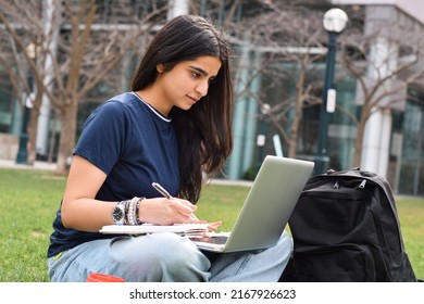 Young Girl Student Sitting On Grass Outside Using Laptop Computer And Writing Notes