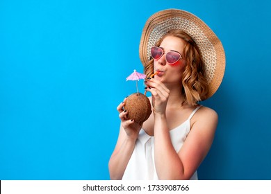 Young Girl In Summer Clothes Drinks A Coconut Cocktail On A Blue Isolated Background, Woman Tourist In A Summer Resort, Summer Concept