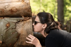 A Young Girl In Sunglasses Engaging With The Natural Environment By Exploring The Scent Of Freshly Cut Tree Trunks In A Forest Setting