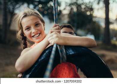 Young girl swinging on a tyre swing in a park. Kids having fun playing on a tyre swing in a park.