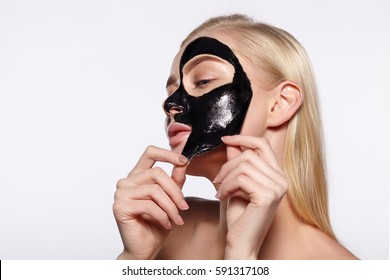 A young girl takes a black mask from her face. The gray background.