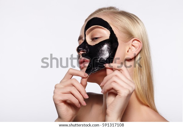 若い女の子が顔から黒いマスクを取る グレイの背景 の写真素材 今すぐ編集