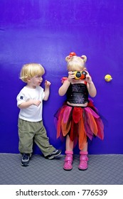 Young Girl Taking A Photo With Disposable Camera With Little Boy Watching And Helping