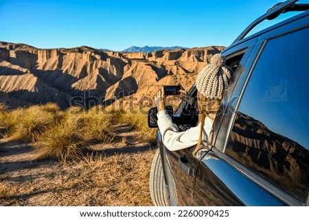 Young girl taking photos of desert landscape through car window.