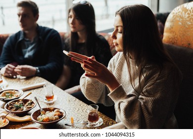 Young Girl Is Taking Pictures Of Food. A Young Company Of People Is Smoking A Hookah And Communicating In An Oriental Restaurant. Lebanon Cuisine Served In Restaurant.  Traditional Meze Lunch