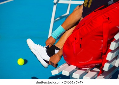 A young girl tennis player is resting while sitting on a bench in between games taking off a sneaker from your foot - Powered by Shutterstock