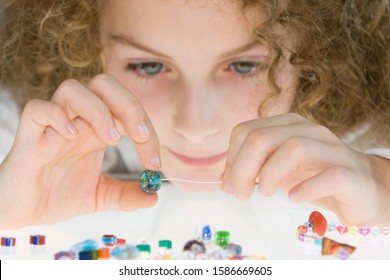 A Young Girl Threading Beads Onto A Thread