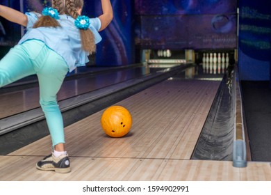 Young Girl Throwing A Ball In Bowling Club. Kid Is Playing Bowling. View From Behind.