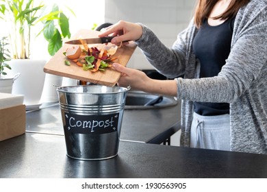 A young girl throws vegetable cuttings in a compost bucket. Metal compost bucket. Women making compost from vegetable leftovers in the modern kitchen. Close up. Recycling, organic garbage. - Shutterstock ID 1930563905