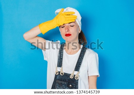 Young girl with a tired and sad face and a handkerchief on her head, holding her head against a blue background. Concept of cleaning and cleaning service, fatigue, hard work, difficult schedule.