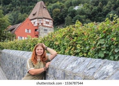 Young Girl Tourist And The Oldest House In The Principality Of Liechtenstein - Red House, Medieval European Architecture And A Vineyard. The Main Attraction Of Liechtenstein, Vaduz.