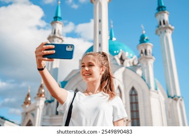 A young girl tourist takes a selfie with a smartphone against the background of a Kul Sharif mosque on a sunny day, Kazan, Russia - Powered by Shutterstock