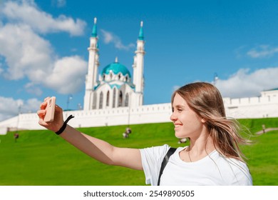 A young girl tourist takes a selfie with a smartphone against the background of a Kul Sharif mosque on a sunny day, Kazan, Russia - Powered by Shutterstock