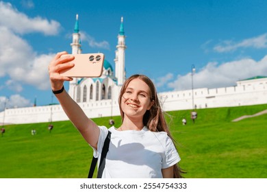 A young girl tourist takes a selfie with a smartphone against the background of a Kul Sharif mosque on a sunny day, Kazan, Russia - Powered by Shutterstock