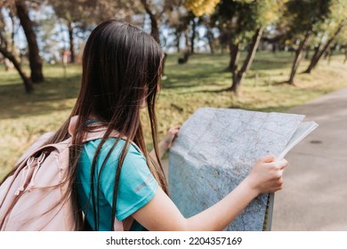 Young Girl Tourist, Wearing Turquoise T Shirt And A Pink Backpack, Checking The Map During Trek In The Park