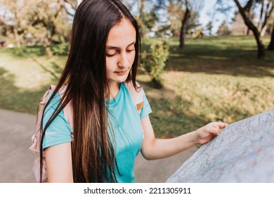 Young Girl Tourist, Wearing Turquoise T Shirt And A Pink Backpack, Checking The Map During Trek In The Park