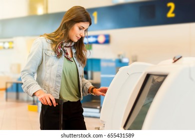 Young Girl Traveller With Trolley Bag Using Self Service Check In Machine At Airport.