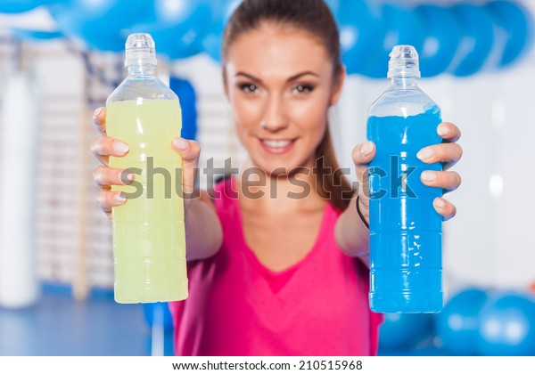 Young girl with two\
isotonic drink (yellow, blue), gym. She is considering which one to\
choose