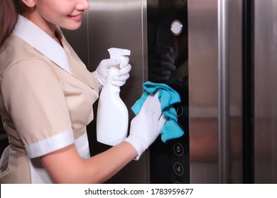 A young girl in uniform wipes the mirror surface of the Elevator. Cleaning service at the hotel. Unrecognizable photo. Cleaning in the hotel Elevator. Copy space.