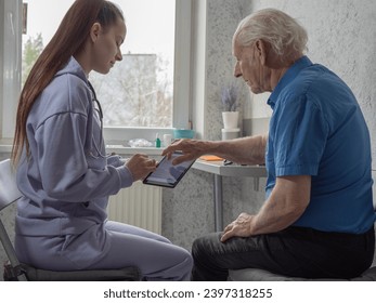 A young girl volunteer helps an old man to master technology, helps and teaches how to use an electronic tablet  - Powered by Shutterstock