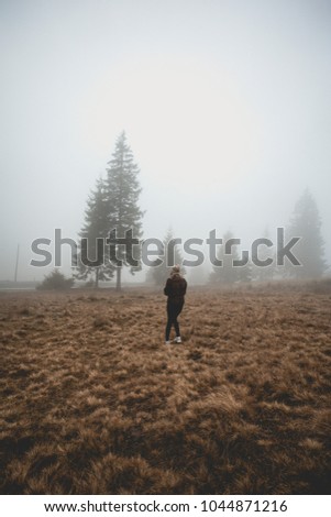 Young girl walking away in a foggy forest path