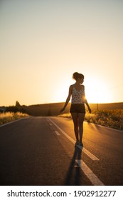 Young girl, walking in the middle of a lonely straight road, late in the day. - Shutterstock ID 1902912277
