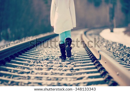 Young girl is walking in the railroad tracks. Image taken during spring time and there is some snow left on the ground. Image has a vintage effect applied.
