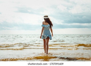 young girl walks along the beach along the sea in a short dress and with a hat