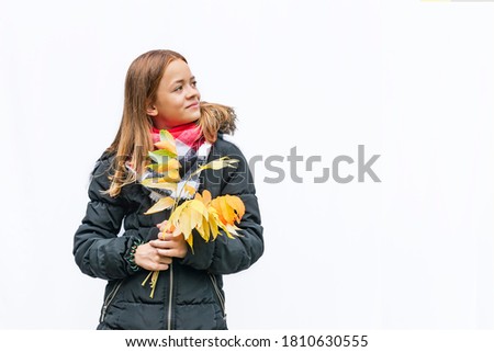 A young girl in a warm jacket with autumn leaves on a white background