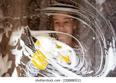 A young girl washes the windows of her house. Homework. Help. Cleaning. View through the window. Lifestile. - Shutterstock ID 2208880511