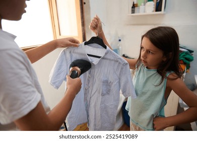 A young girl watches as a shirt is steamed using a garment steamer in a home setting, showcasing domestic chores. - Powered by Shutterstock