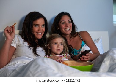 Young Girl Watching TV In Bed With Gay Female Parents