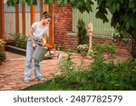 A young girl is watering plants in a garden. She is wearing a white shirt and blue jeans