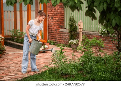 A young girl is watering plants in a garden. She is wearing a white shirt and blue jeans - Powered by Shutterstock