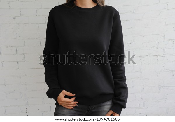 Young  girl wearing black\
template women\'s sweatshirt with copy space for your design or\
logo, mock-up of black cotton sweatshirt, white stone wall in the\
background.