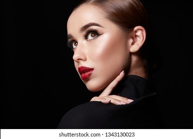 Young girl wearing evening make up with red lips and long lashes at black studio background. 