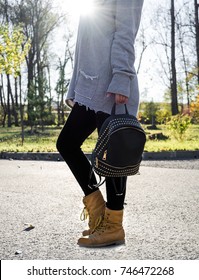 Young Girl Wearing Gray Sweatshirt, Black Yoga Pants And Brown Boots Is Holding A Black Backpack With Rhinestones. Casual Style.