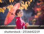 Young girl wearing Kimono, traditional Japanese costume, takes pictures of red autumn leaves in Kyoto.