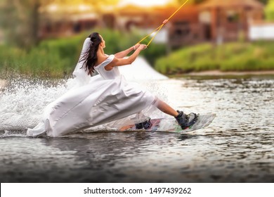 A young girl in a wedding dress riding on a wakeboard on the lake. Extreme bride. Unusual bride. An extraordinary bride.