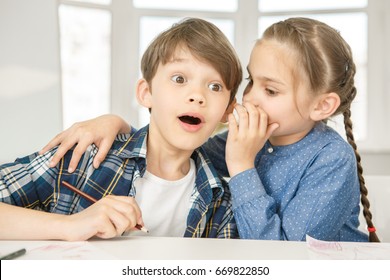 Young girl whispering to a boy shocking news. Cute little boy looking surprised listening to his friend whisper something to his ear children secrets gossip news overwhelmed shock surprise emotions - Powered by Shutterstock