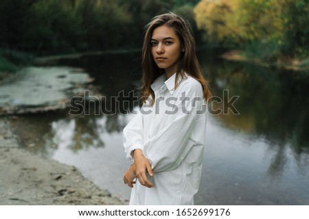 
A young girl in a white dress walks barefoot on a river in a forest in blue Holi paint