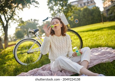A young girl in white making bubbles and looking enjoyed