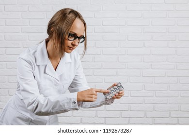 A young girl in a white robe holds a medication in her hand and shows them against a white background - Powered by Shutterstock