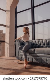  young girl in white shirt and jeans is sitting and relaxing with smile in sunlights in blue sofa near panoramic windows  background, lifestyle concept	, free space
