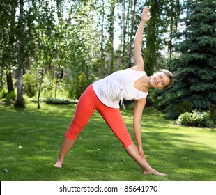 Young Girl In A White Shirt And Red Pants Doing Yoga Outdoors