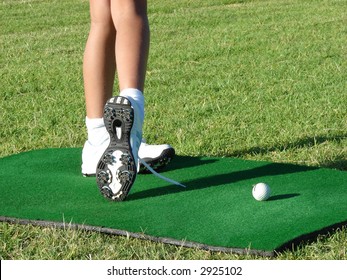 Young Girl In White Shoes Standing On A Practicing Mat During Golf Lesson, Holding A Golf Club