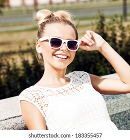 young girl in white summer dress wearing sunglasses smiles for the camera